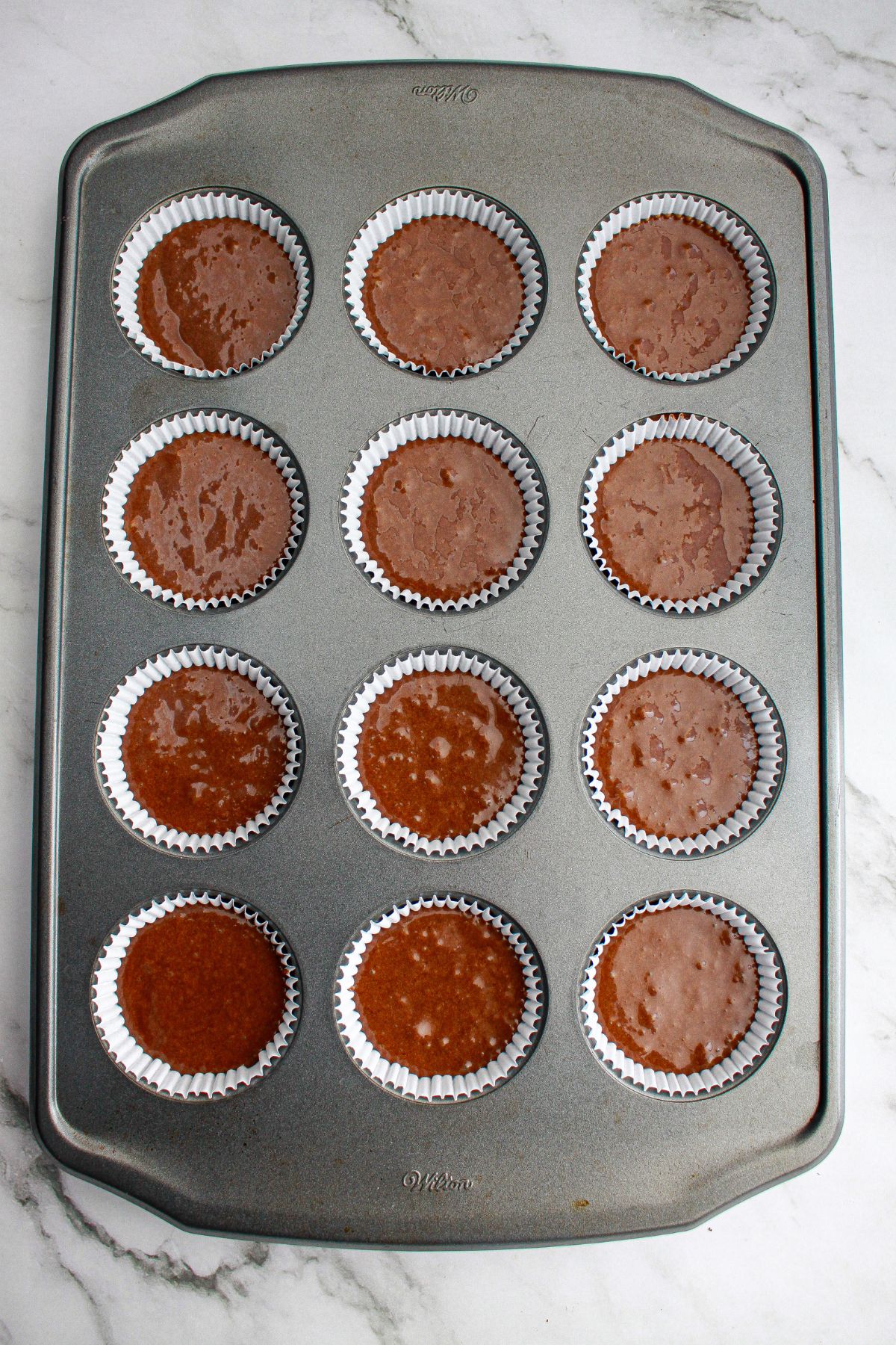 raw cupcake batter in a cupcake lined baking sheet ready for the oven.
