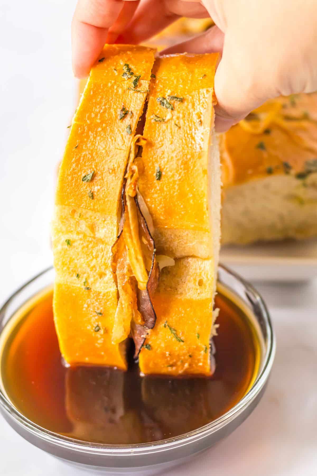 slice of french dip pull apart bread being dipped into a small bowl of au jus.