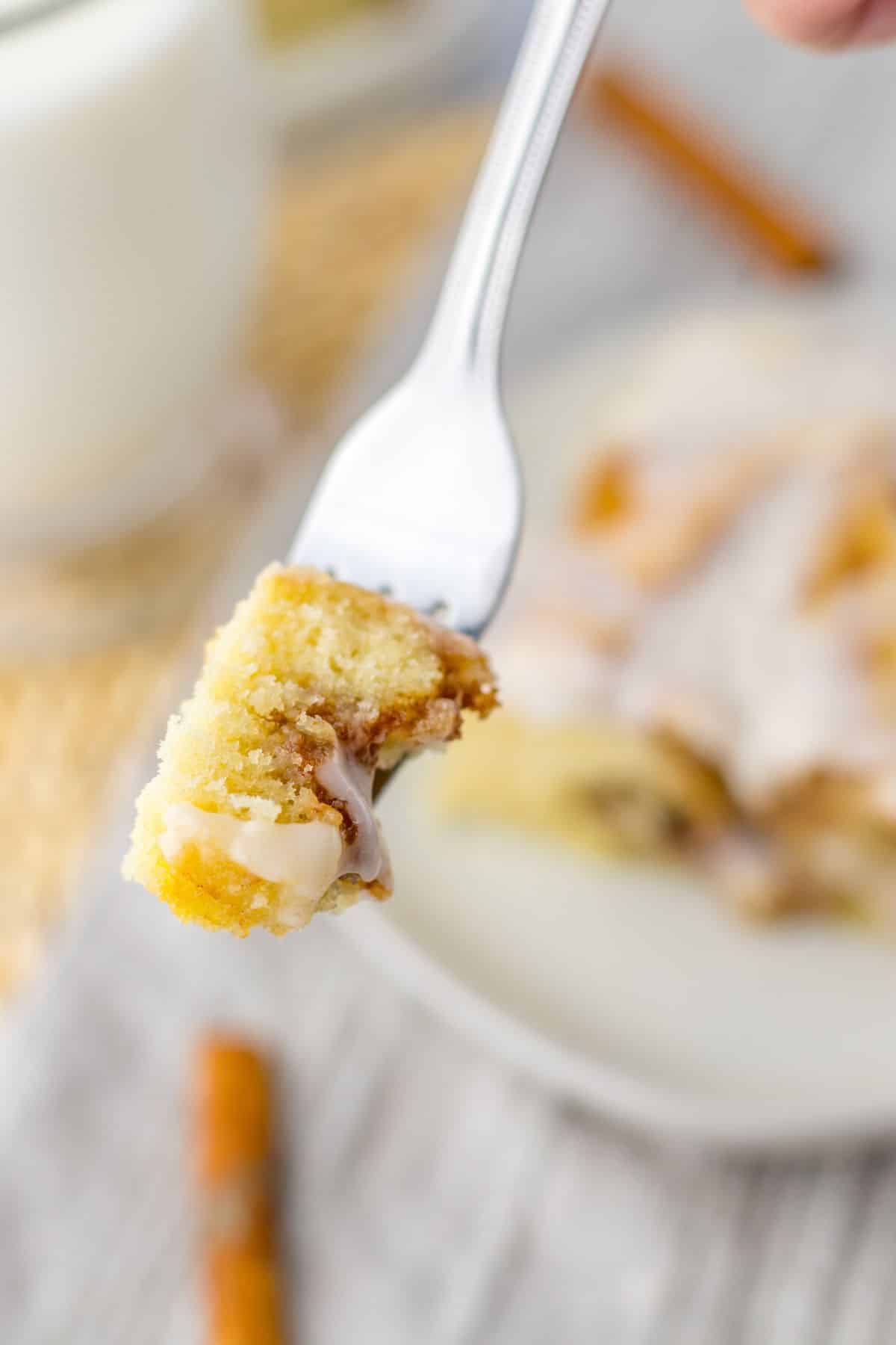 piece of ooey gooey cinnamon roll cake on a fork held in the air.