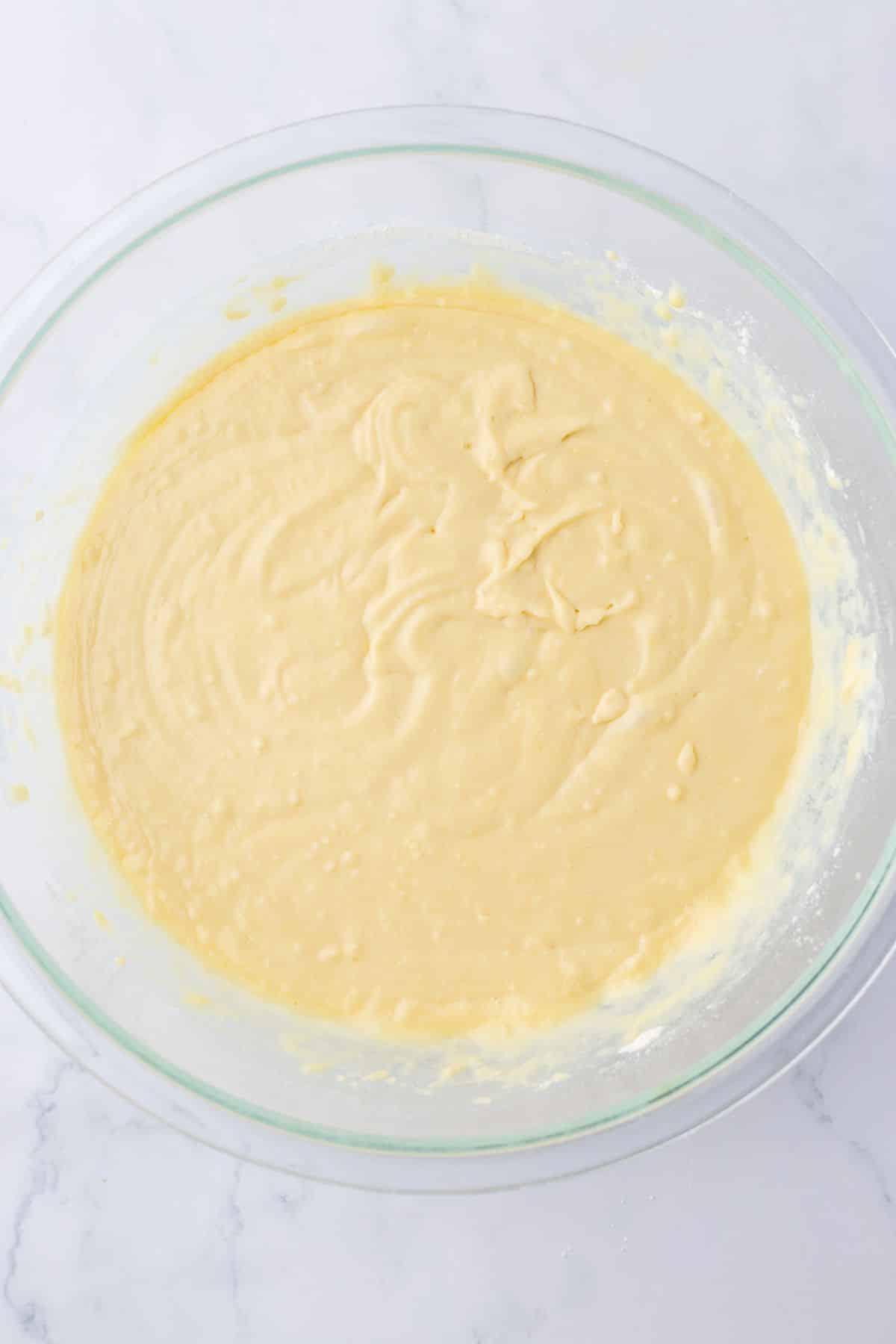cake batter being mixed in a glass mixing bowl.