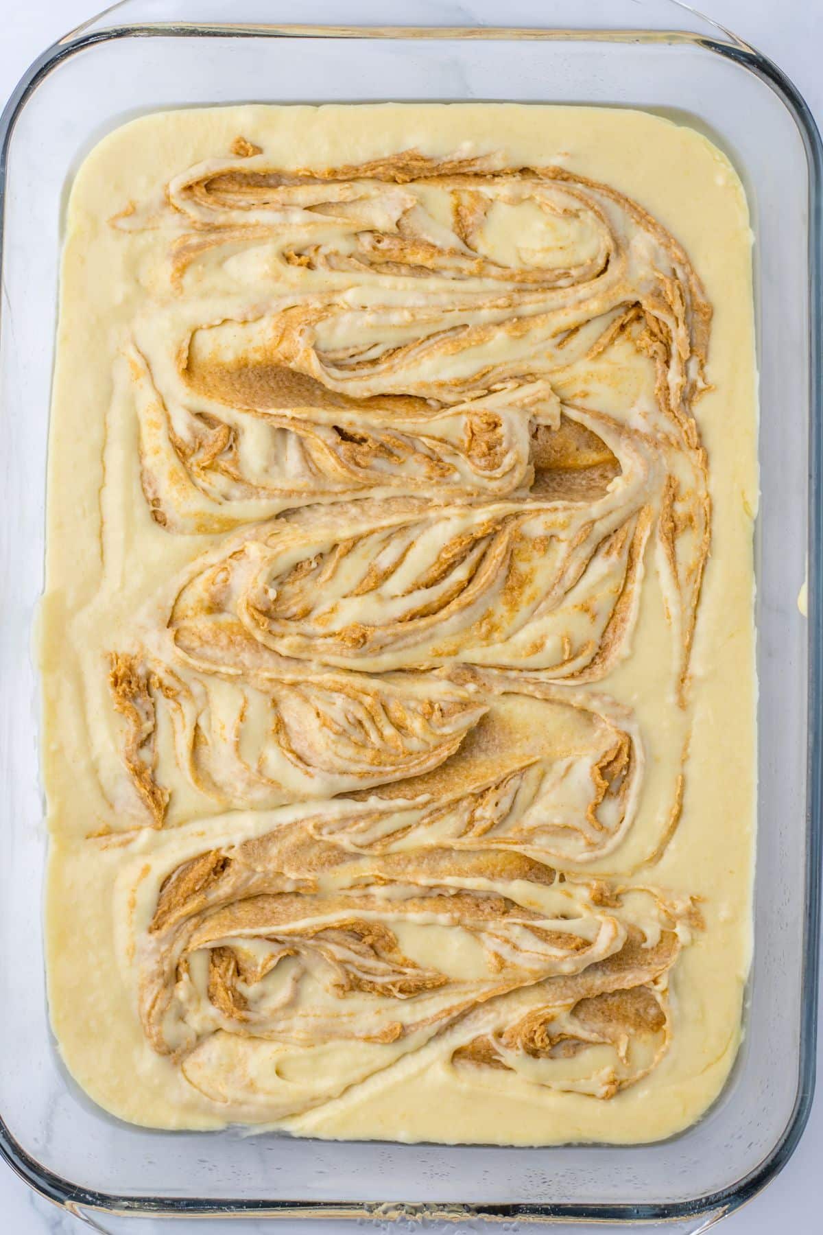cinnamon sugar mixture being swirled into cake mix in a glass baking dish.