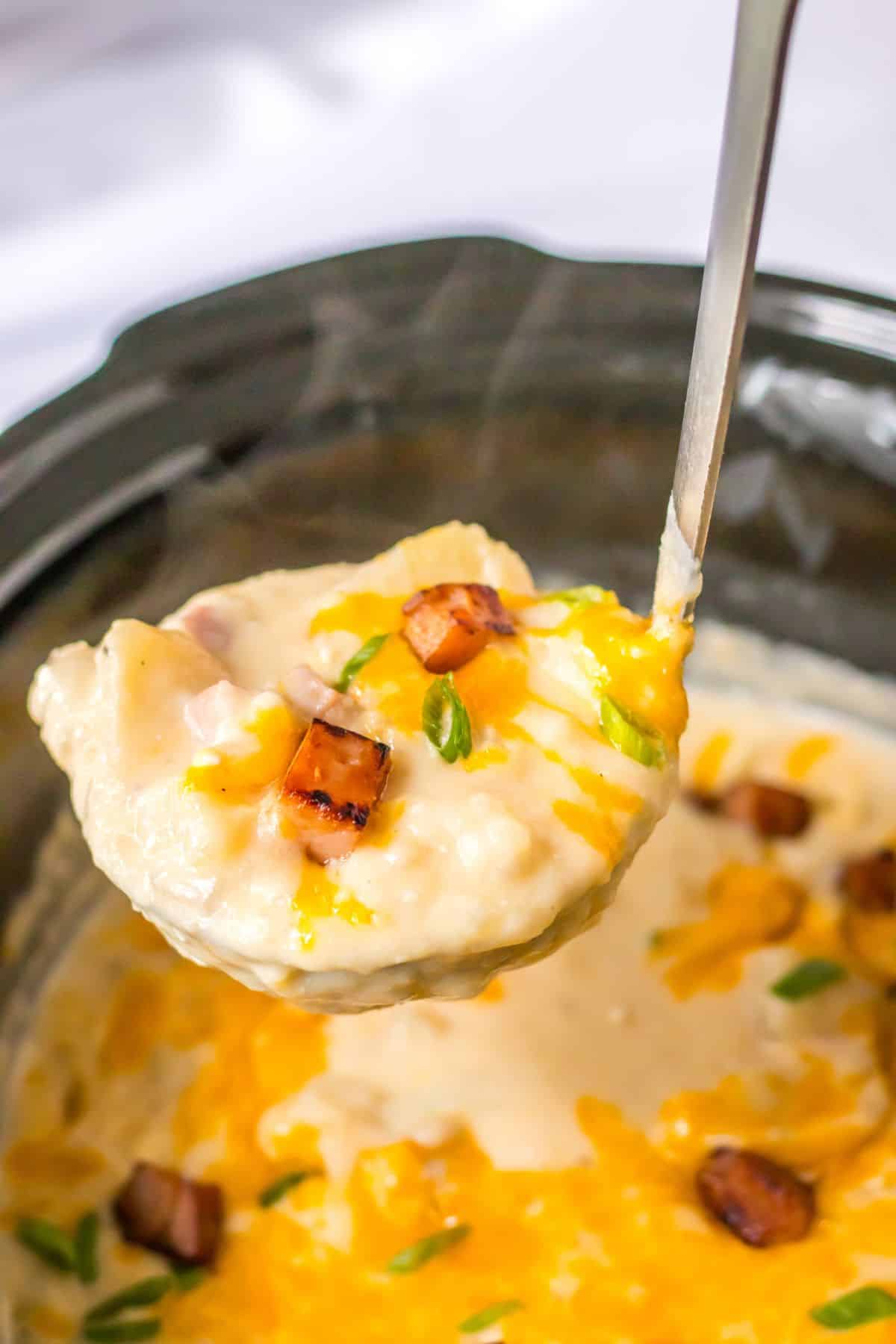 spoonful of ham potato soup held in the air above a slow cooker.