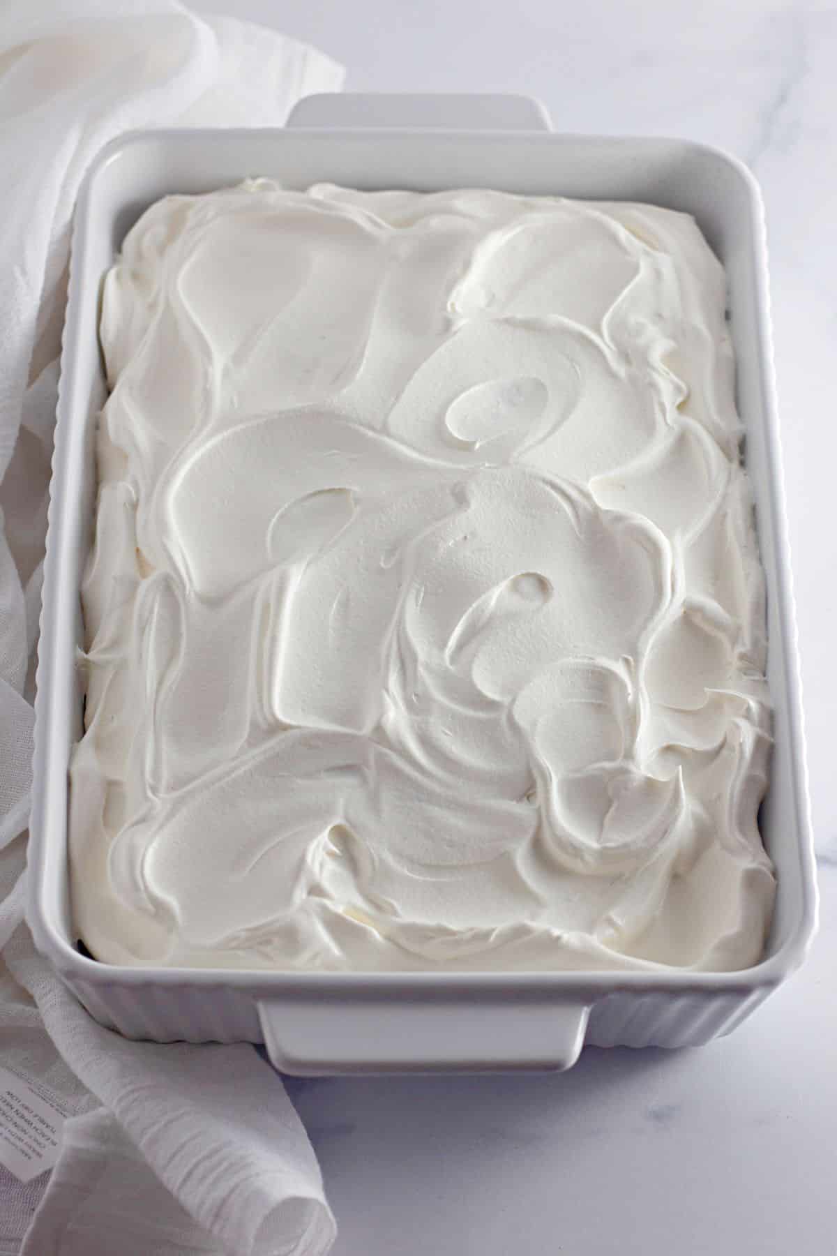 cool whip being spread on top of a cake in a casserole dish.