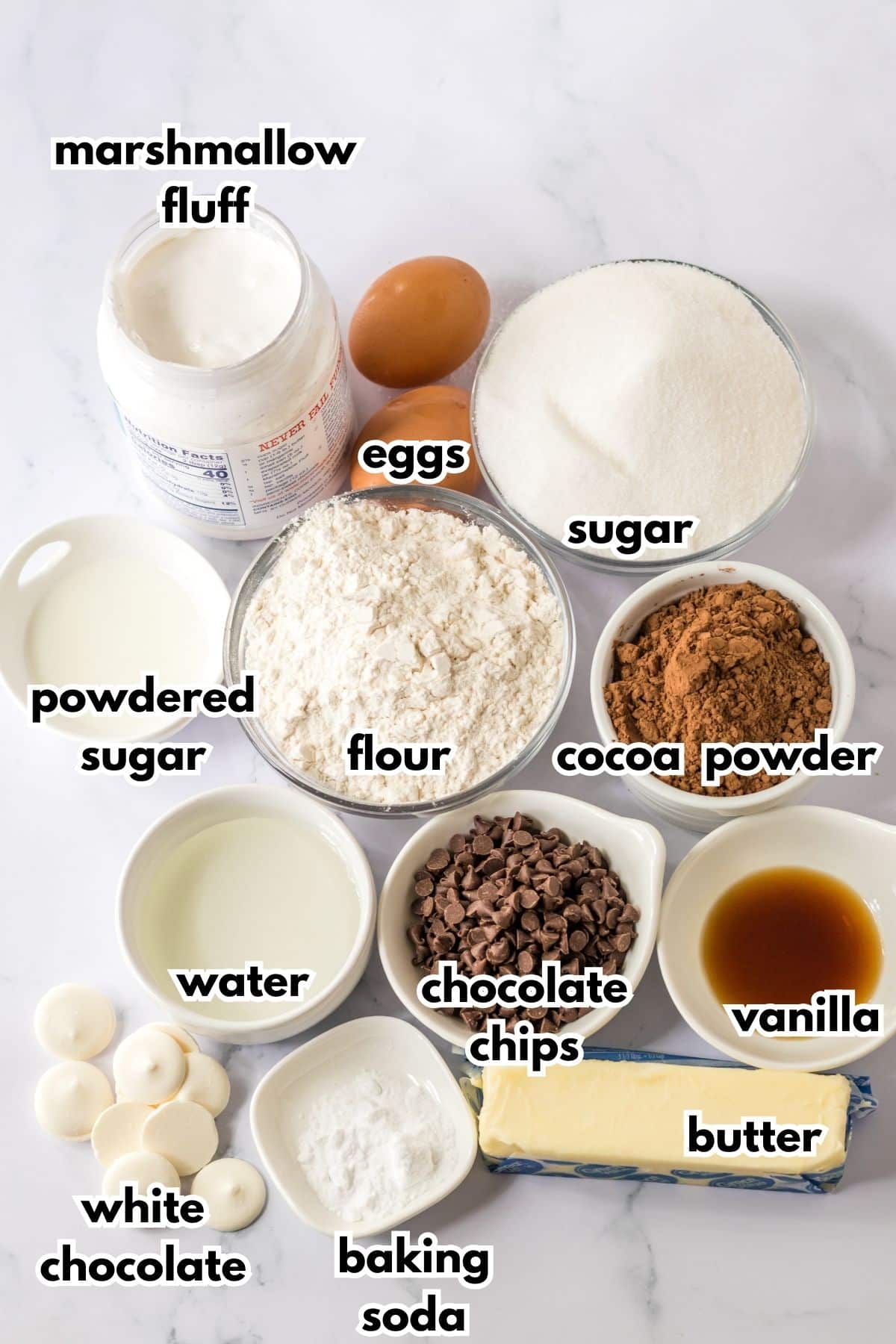 bowls of marshmallow fluff, egg, sugar, powdered sugar, flour, cocoa powder, water, chocolate chips, vanilla, white chocolate, baking soda, and butter on a counter.