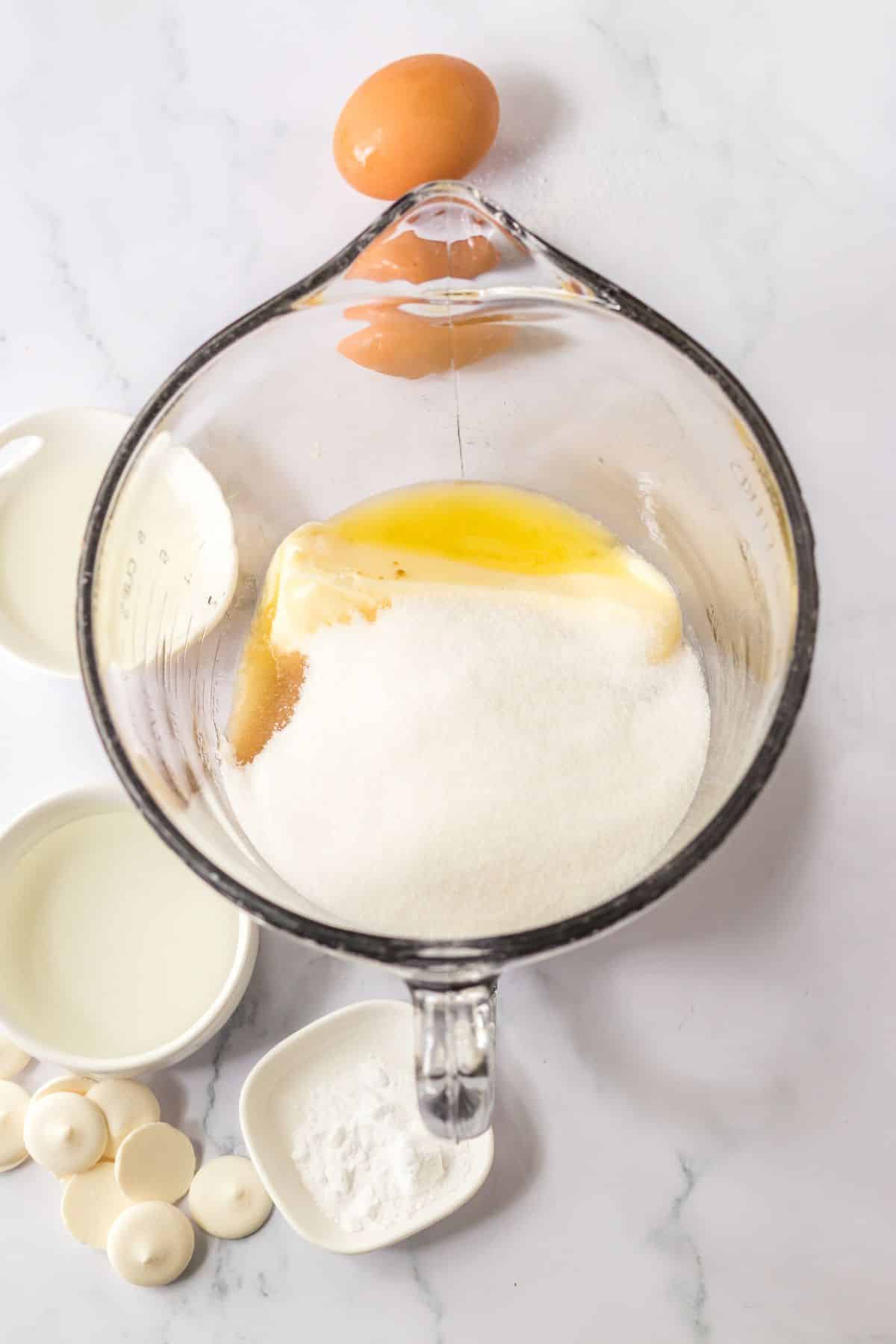 butter, sugar, and vanilla being mixed in a glass mixing bowl.