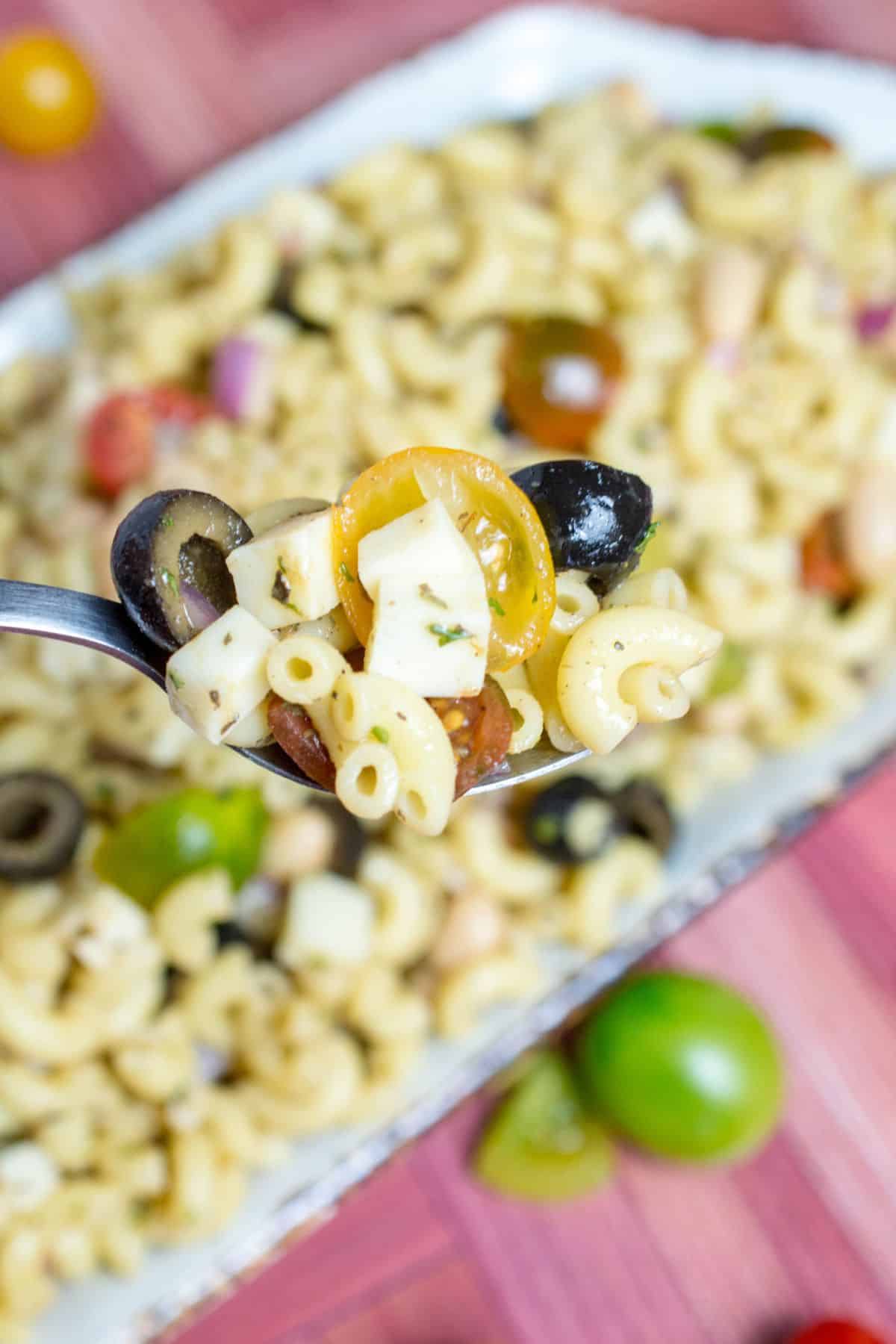 spoonful of italian pasta salad held in the air over a serving tray.