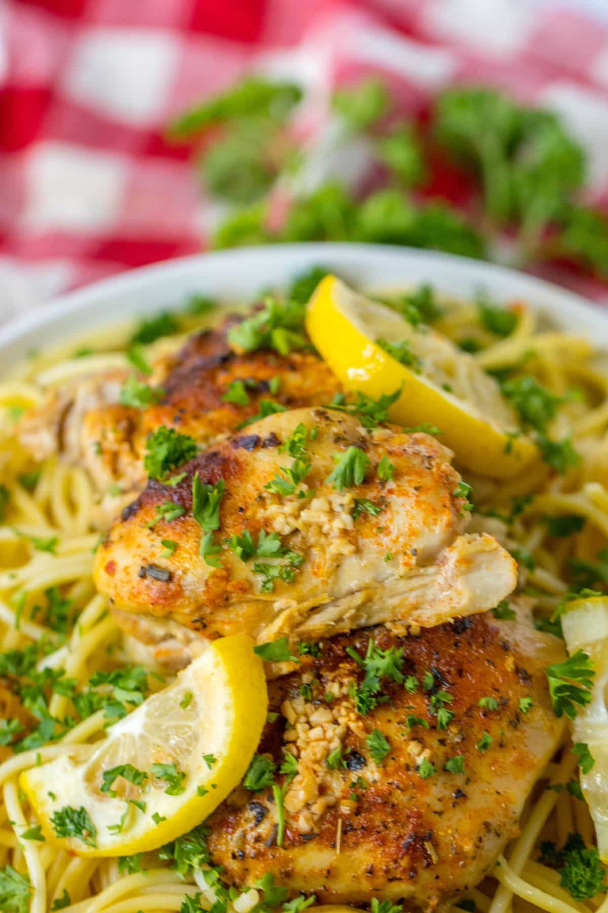 bowl full of spaghetti noodles and topped with slow cooker lemon chicken thighs.