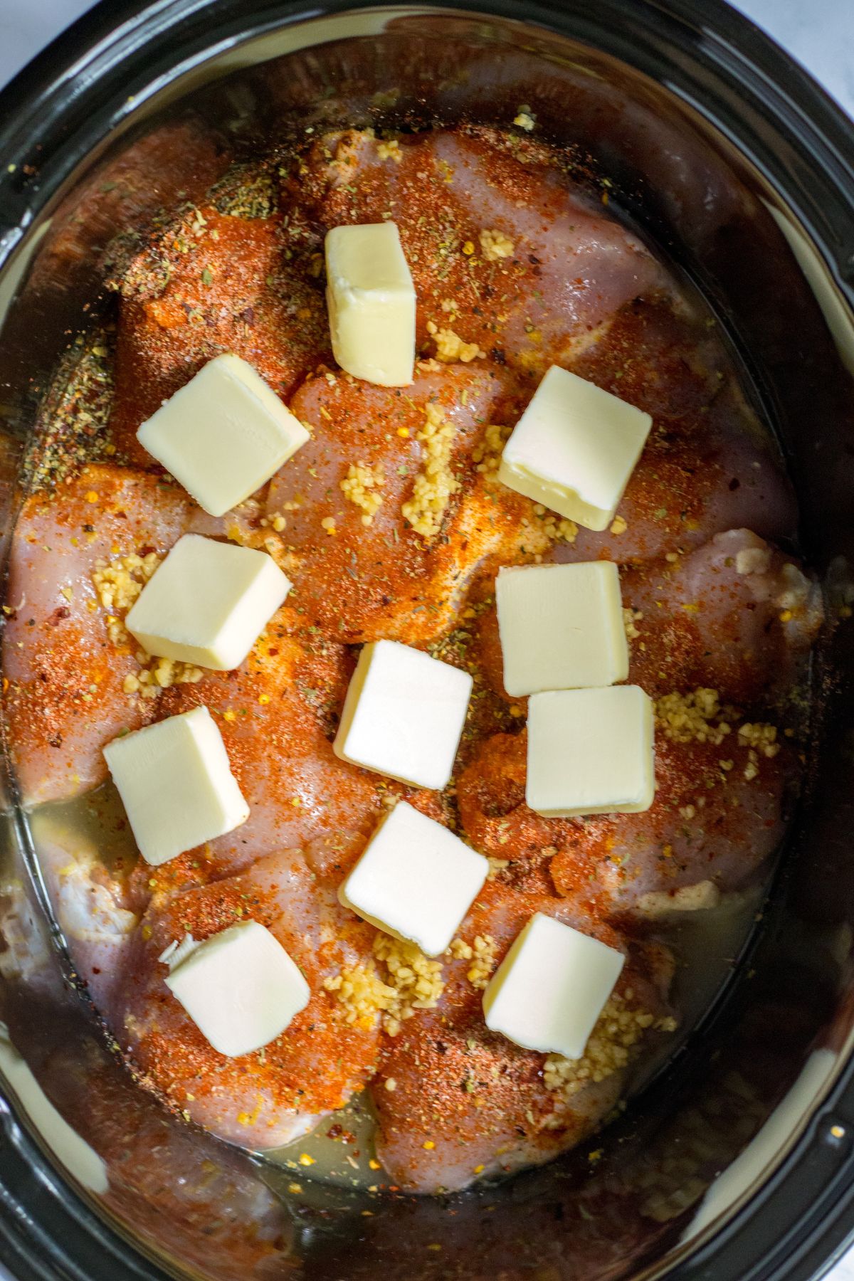chicken thighs coated in seasonings and topped with pats of butter in a slow cooker.