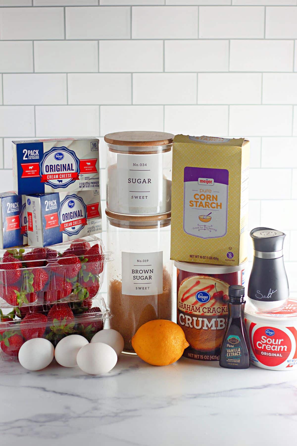 containers of cream cheese, strawberries, eggs, lemon, vanilla, salt, sour cream, sugar, brown sugar, cornstarch, and graham cracker crumbs.