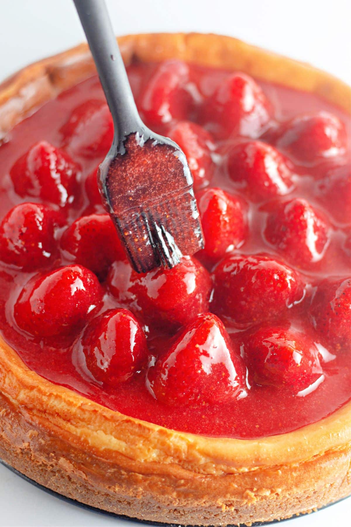 strawberry glaze being brushed on top of a baked cheesecake.