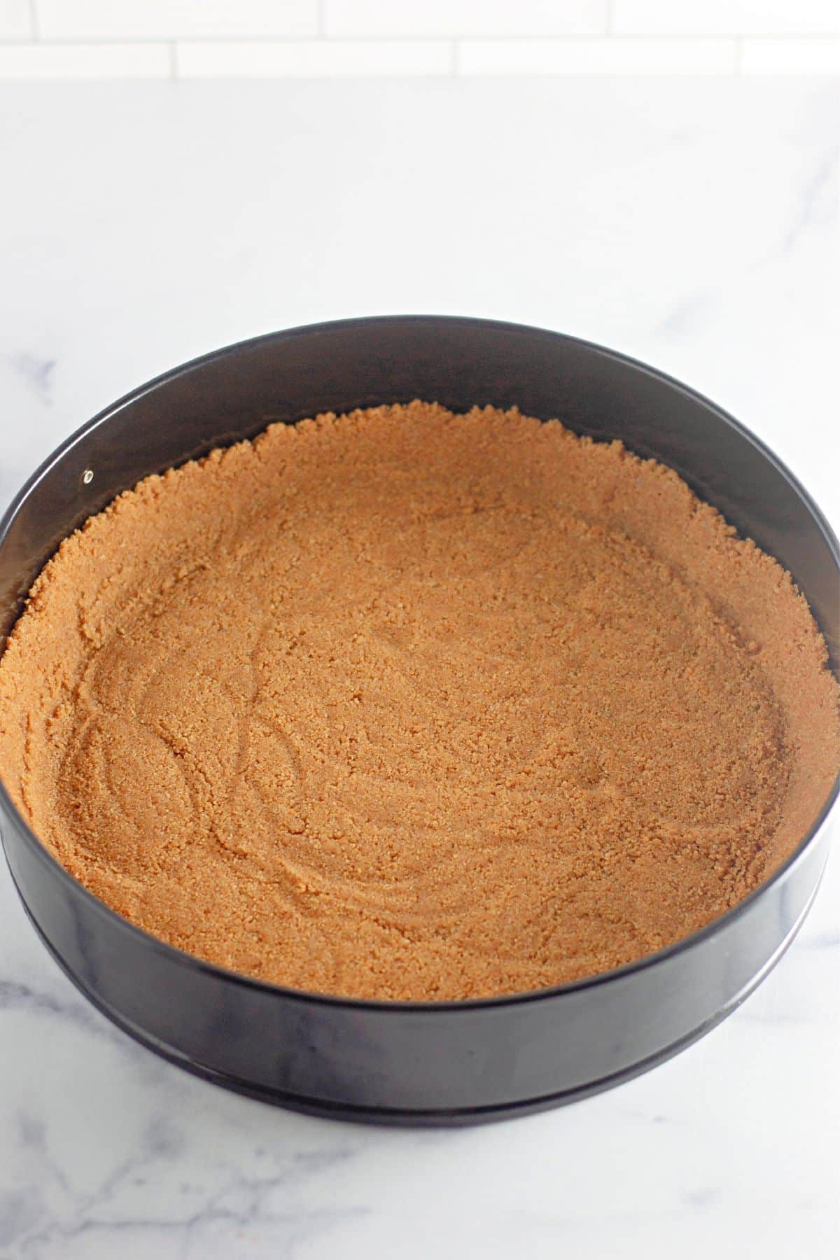 graham cracker crust being pressed into a springform pan.