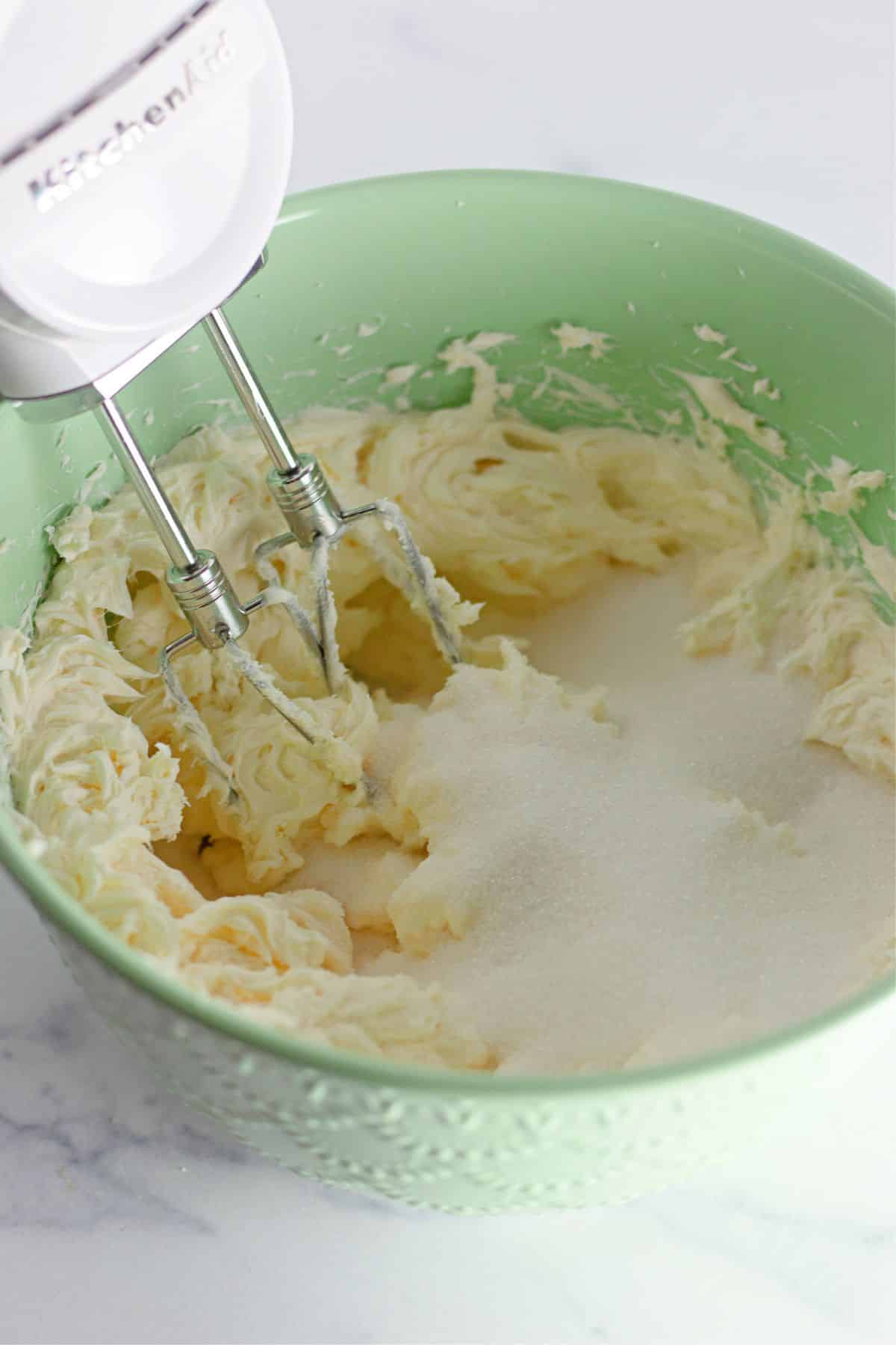 cream cheese and sugar being mixed in a large mixing bowl with a hand mixer.