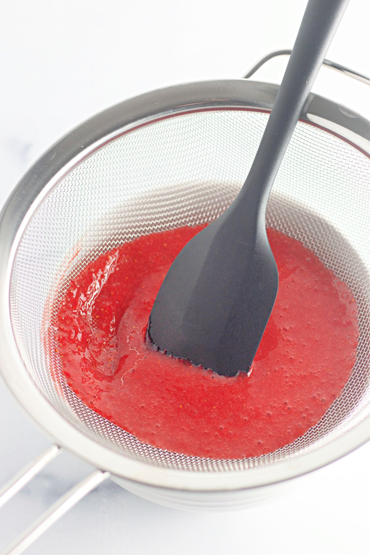 strawberry puree being stained in a fine mesh strainer.