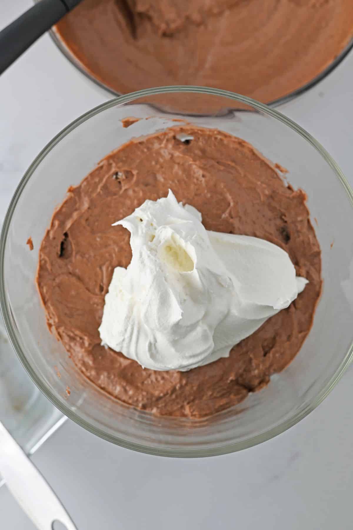 oreo brownie trifle being layered in a trifle bowl.