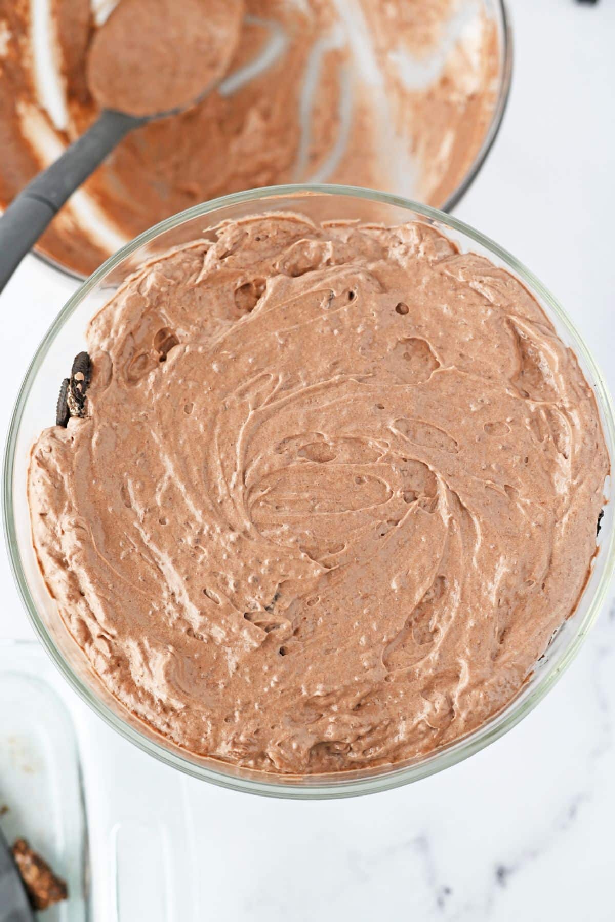oreo brownie trifle being layered in a trifle bowl.