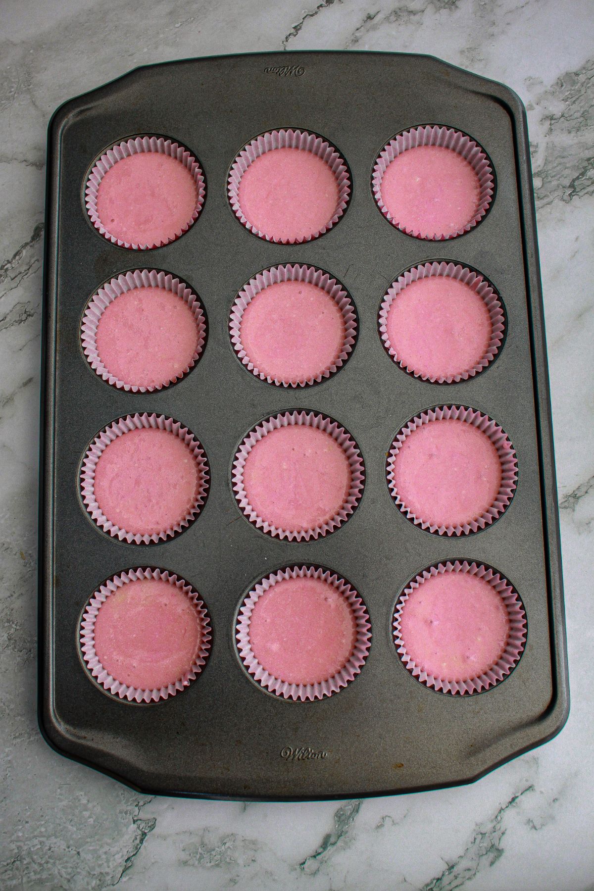 pink cupcake batter in a muffin pan ready for the oven.
