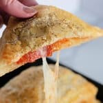 puff pastry pizza pockets on a plate with one held in a woman's hand.