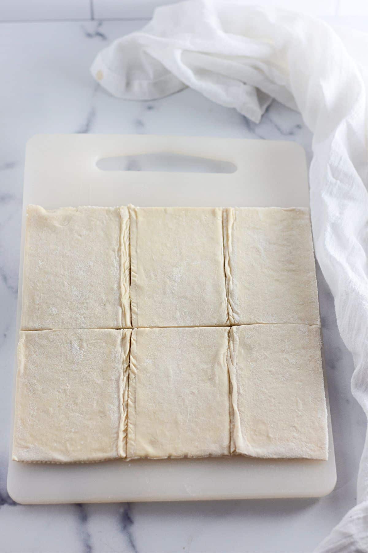 puff pastry dough being rolled out and cut on a cutting board.