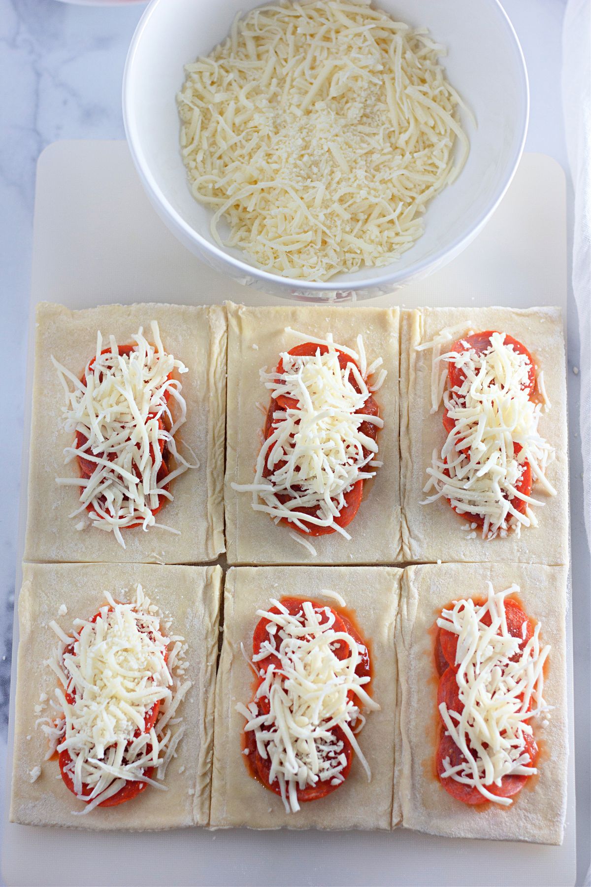 puff pastry being filled with pizza sauce, mozzarella cheese, and pepperoni.