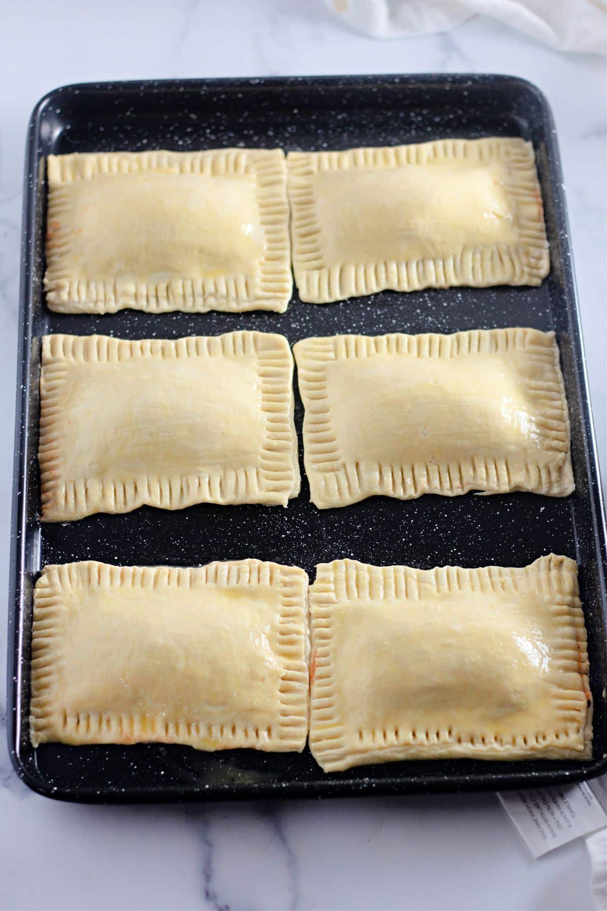 puff pastry pizza pockets being brushed with egg wash on a baking sheet.