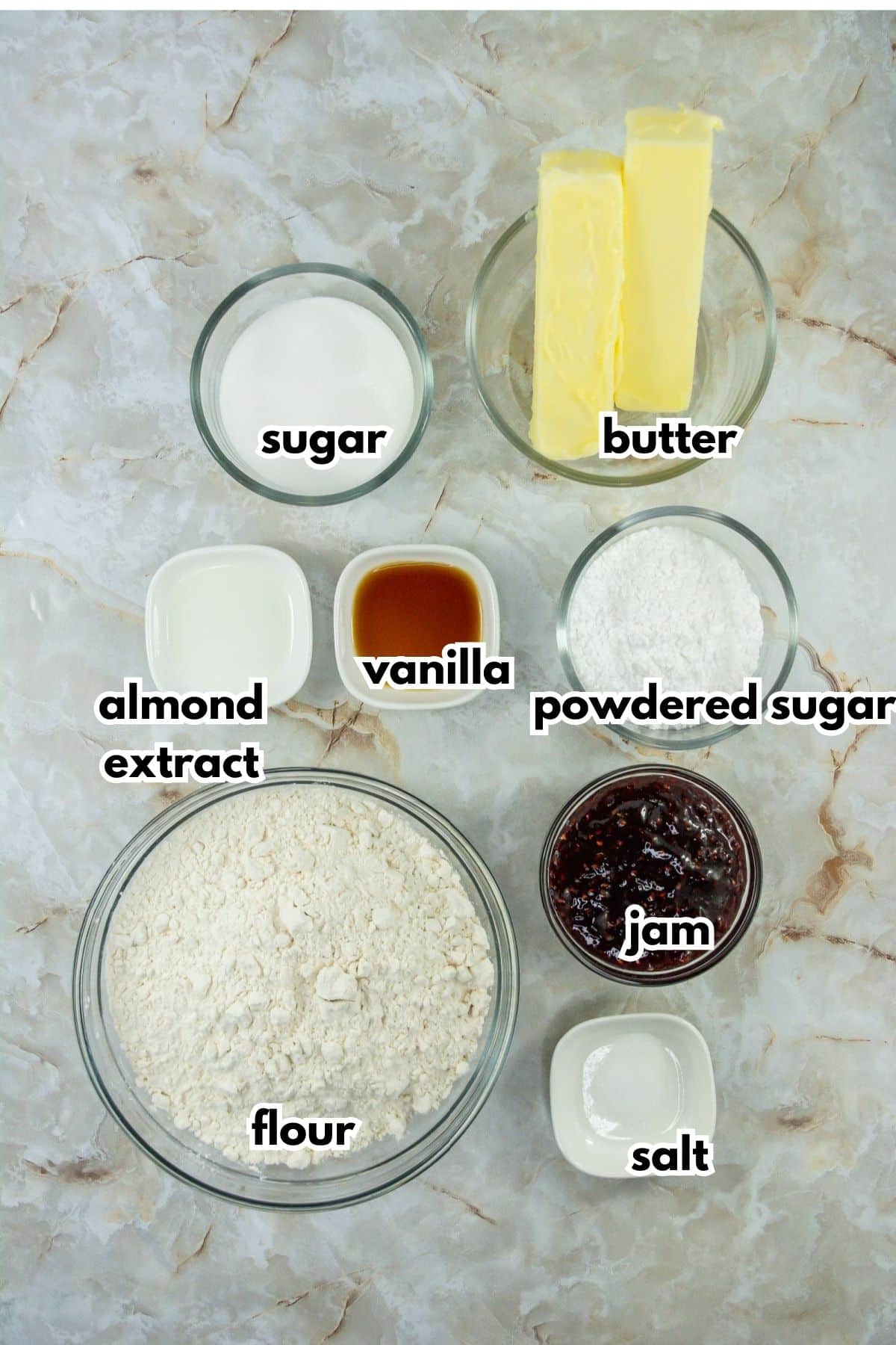 bowls of sugar, butter, almond extract, vanilla extract, powdered sugar, flour, jam, and salt on a counter.