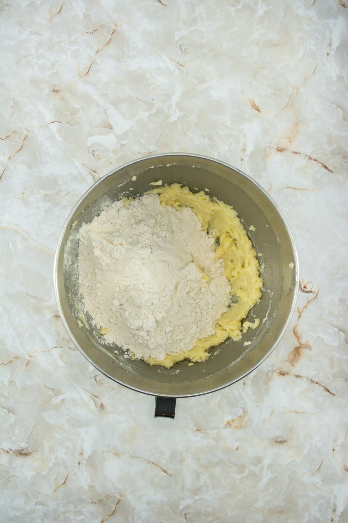 flour and salt being added to creamed butter and sugar in a stainless steel mixing bowl.