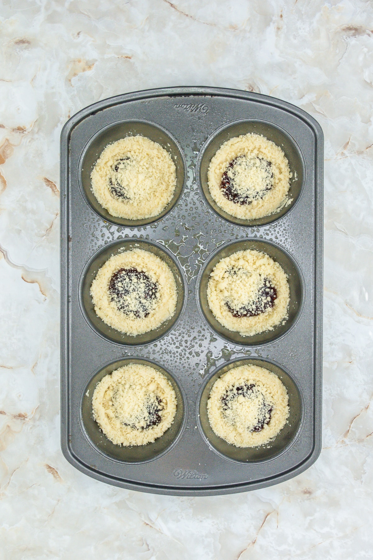 dough being pressed into the bottom of the muffin pan, and then filled with raspberry jam.