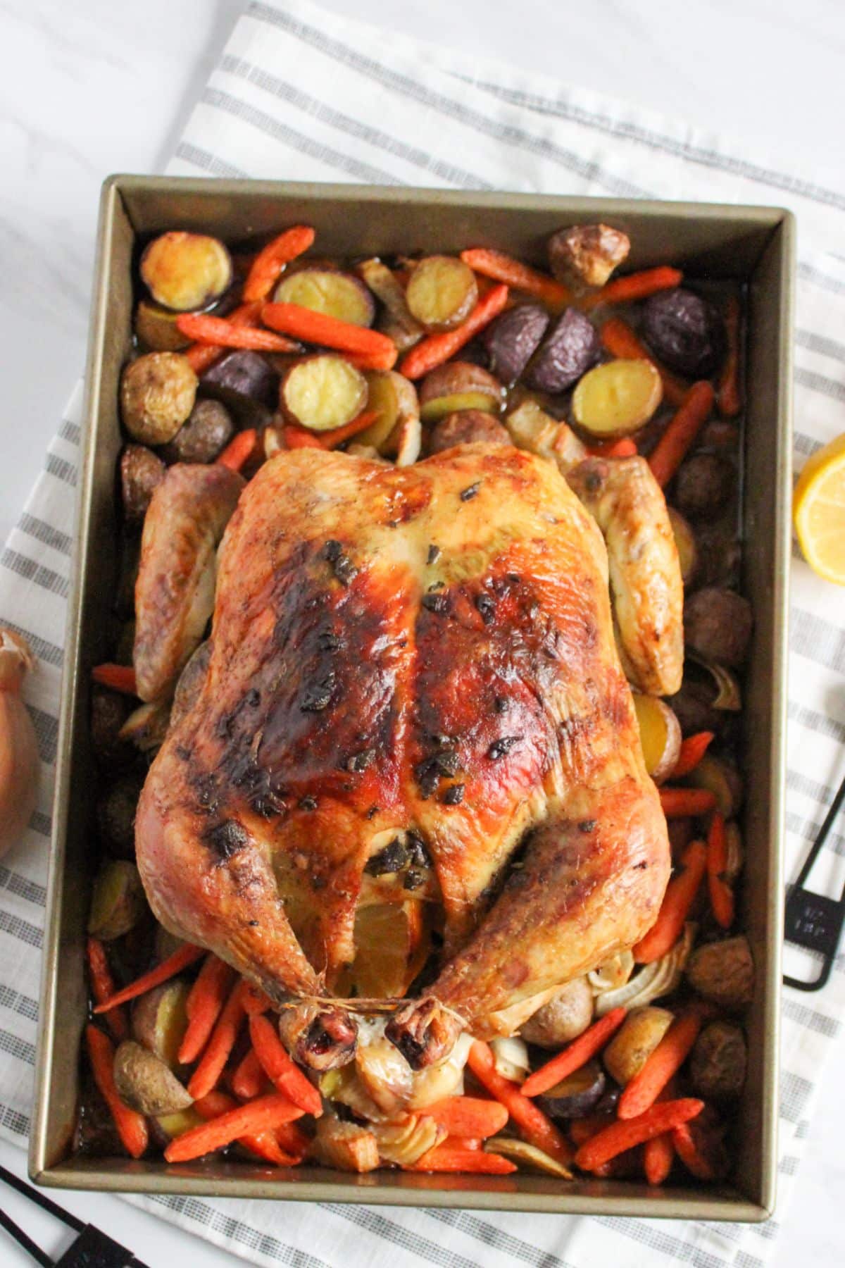 finished roasted chicken on top of a bed of potatoes, carrots and onions.
