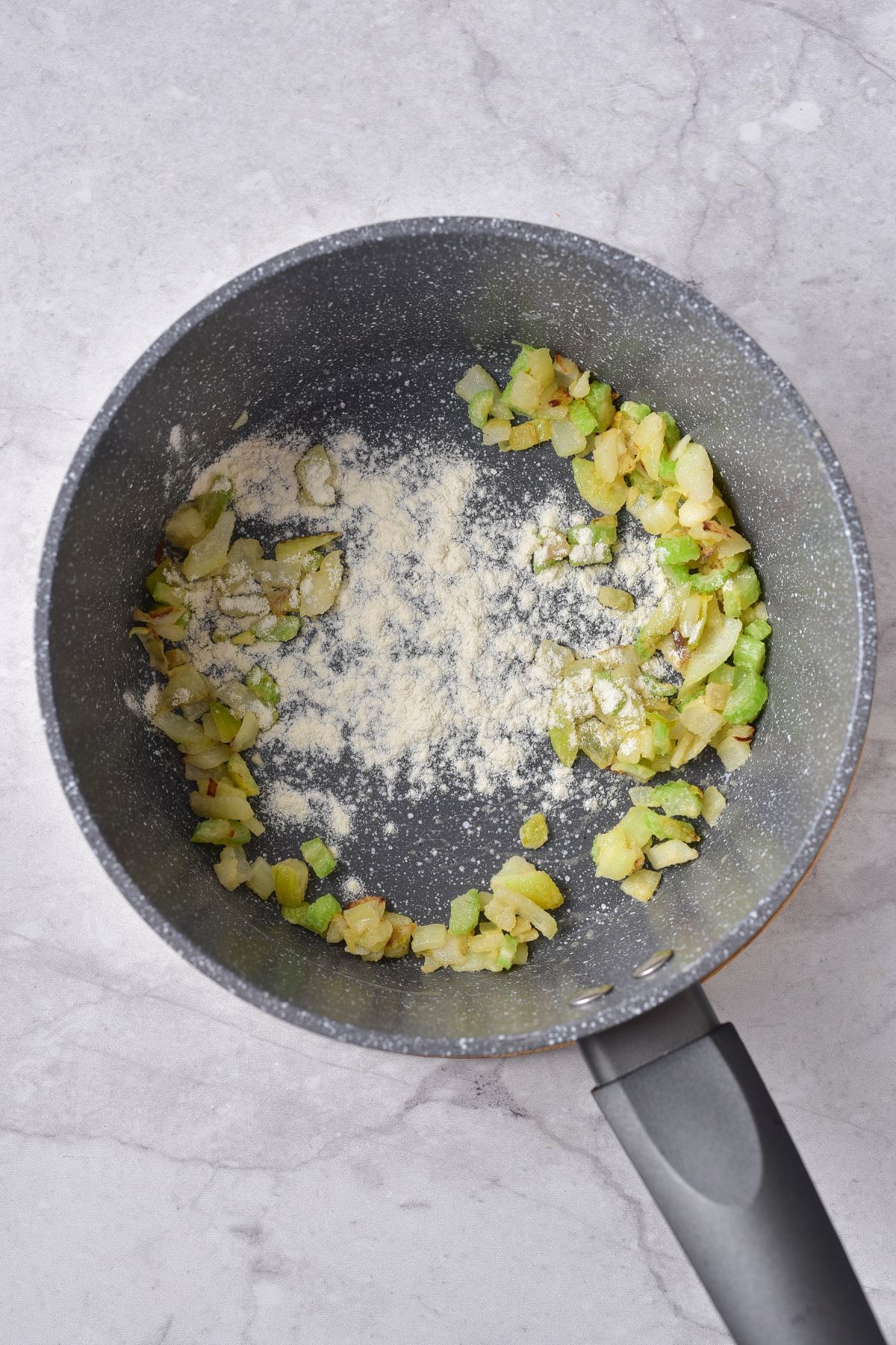 flour being added to cooked onion and celery in a pot.