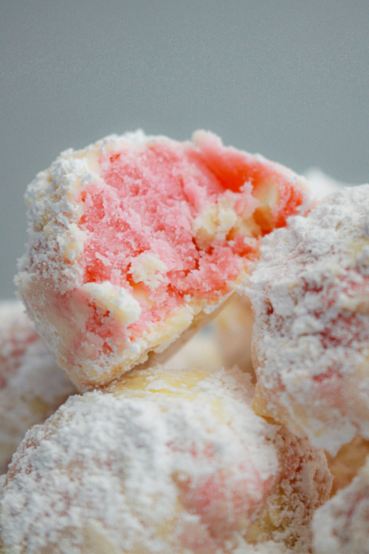 stack of strawberry snowball cookies with the top cookie bitten in half.