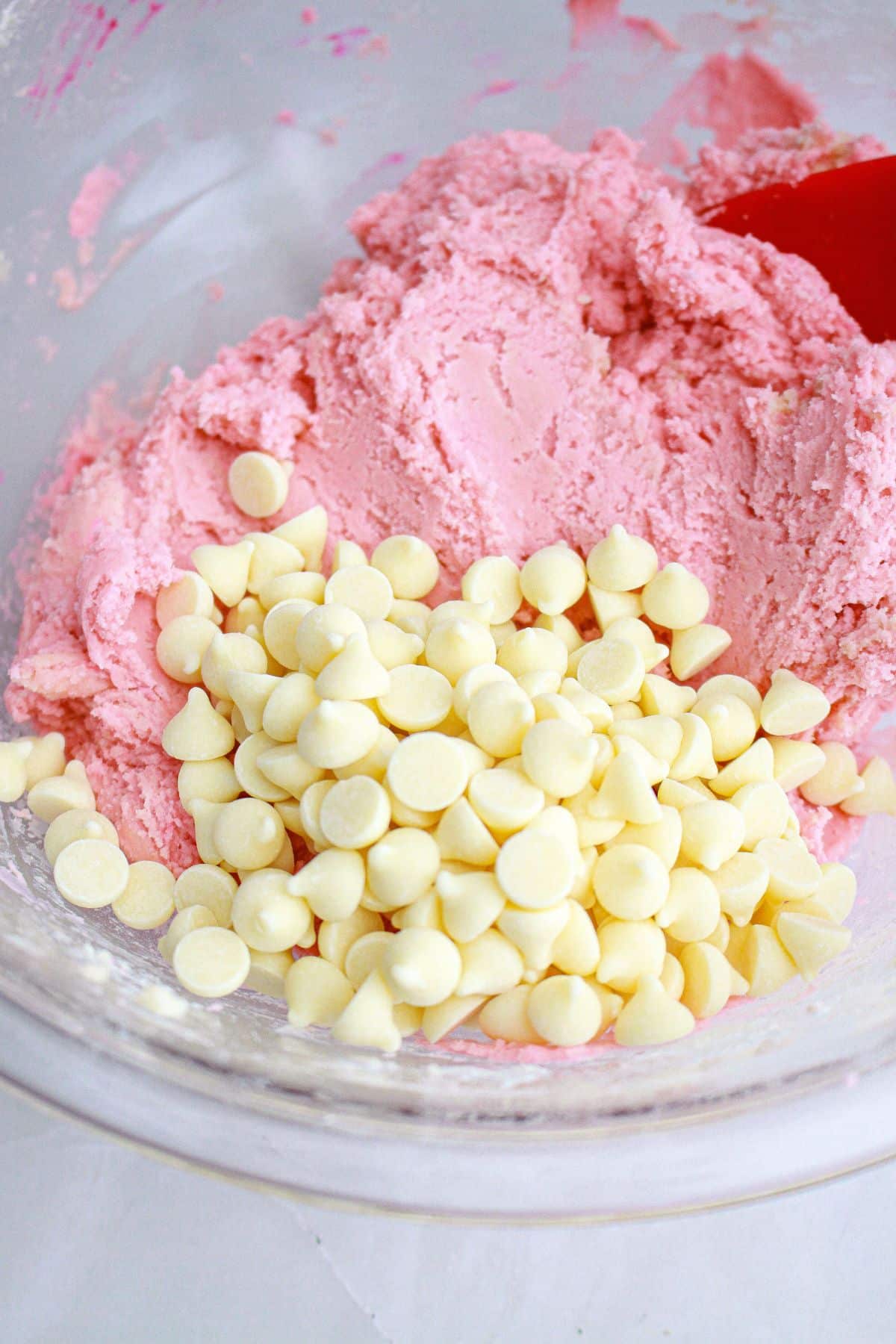 white chocolate chips being stirred into strawberry cookie dough. 