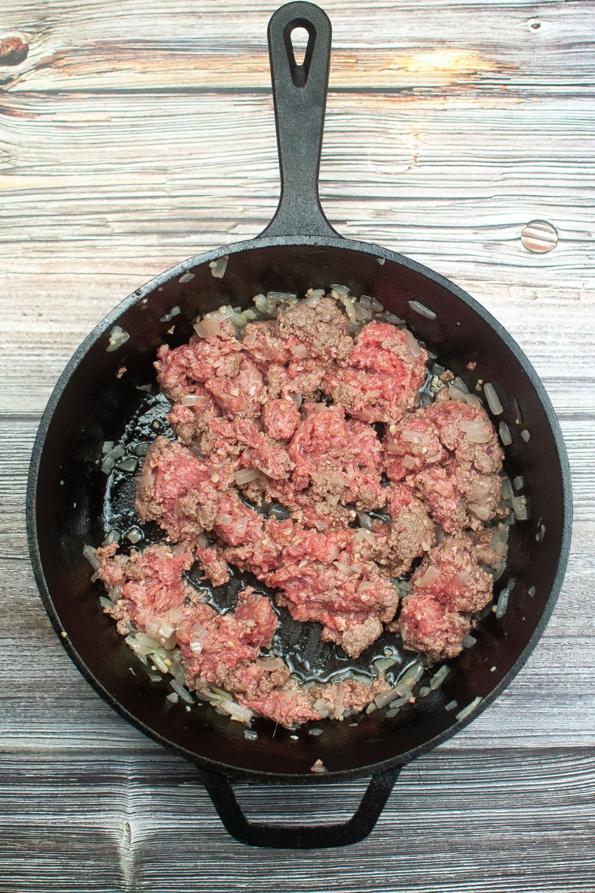 ground beef and onions being cooked together in a cast iron skillet.
