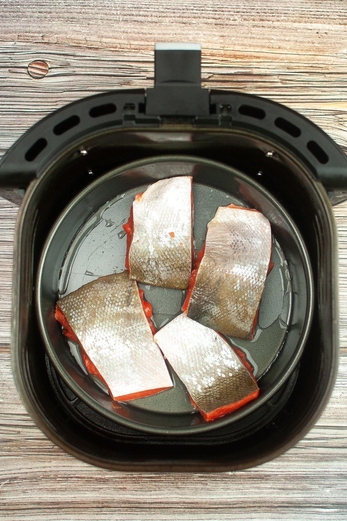 slices of skin on salmon fillets in a baking pan inside the air fryer basket.