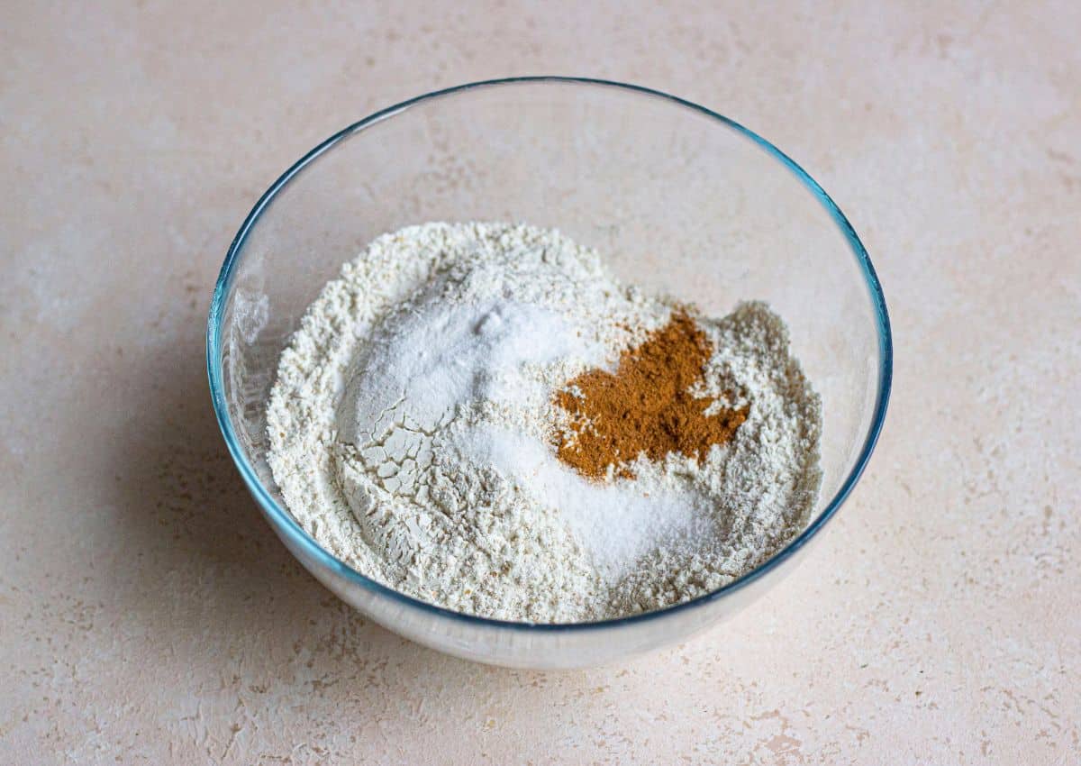 flour, baking soda, salt, and cinnamon being mixed a in glass bowl.