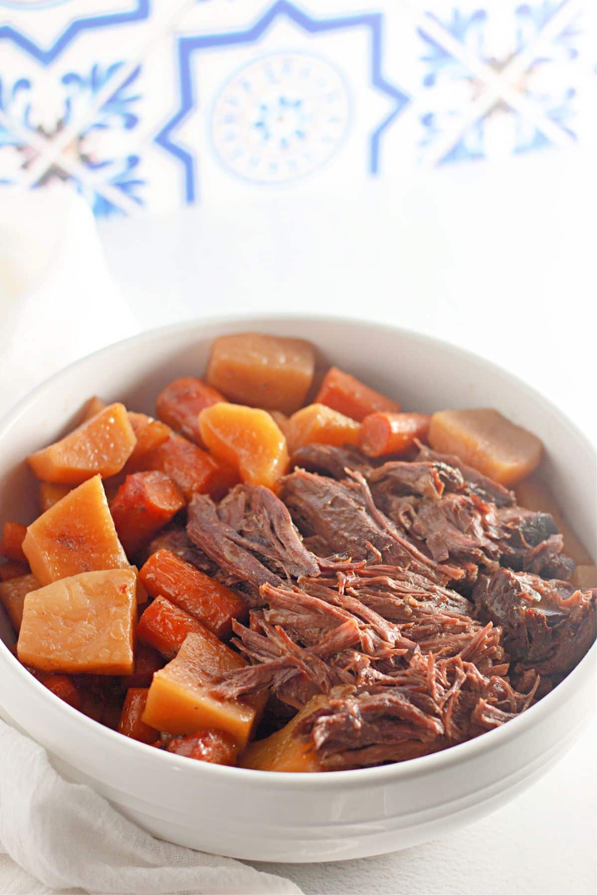 bowl full of pot roast, potatoes and carrots on a counter.
