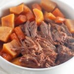 bowl full of pot roast, potatoes and carrots on a counter.