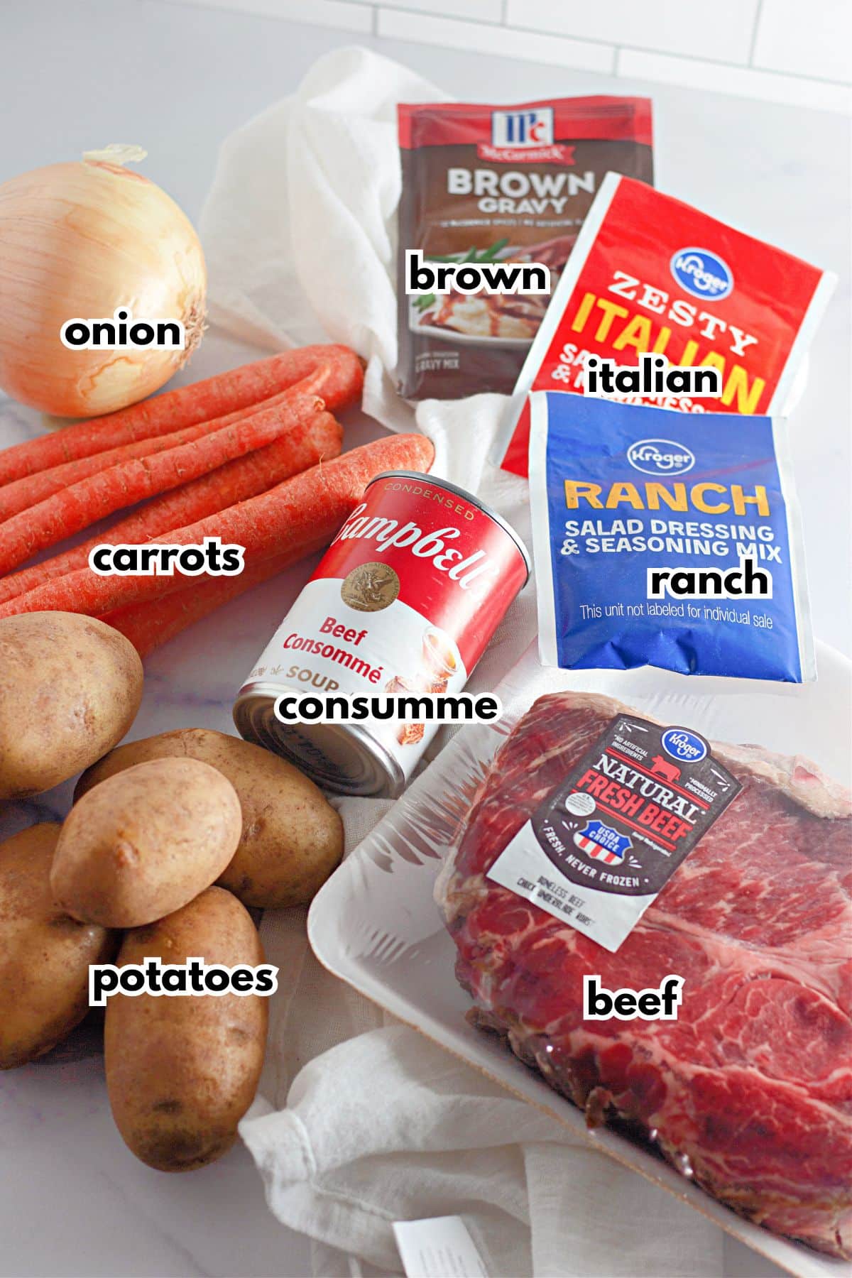 onion, carrots, potatoes, consummer, beef, brown gravy, italian seasoning, and ranch seasoning on a counter.
