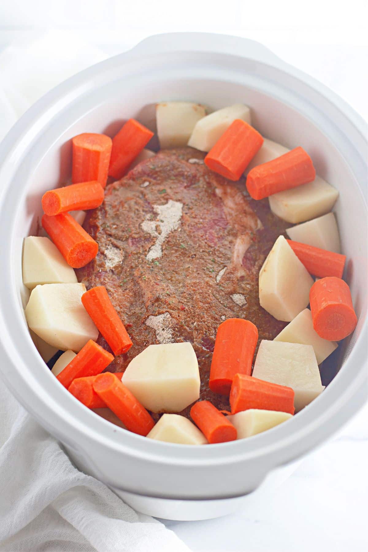 raw potatoes, carrots, and beef roast in a slow cooker.