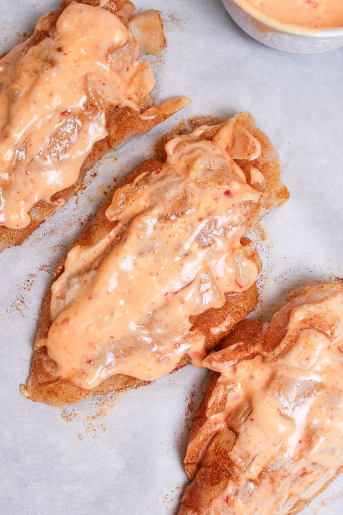 sauce being spread on seasoned chicken breasts.