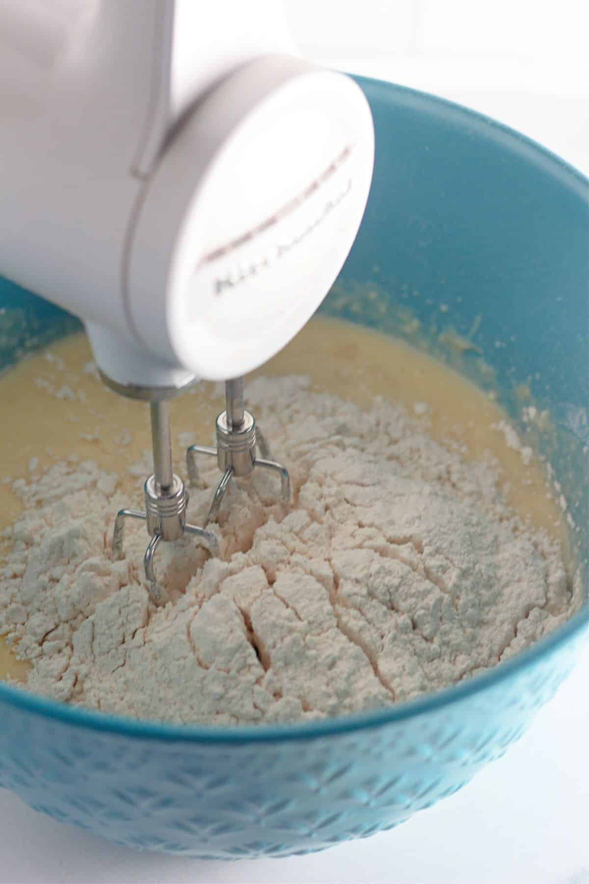dry ingredients being mixed into the cake batter with a hand mixer.