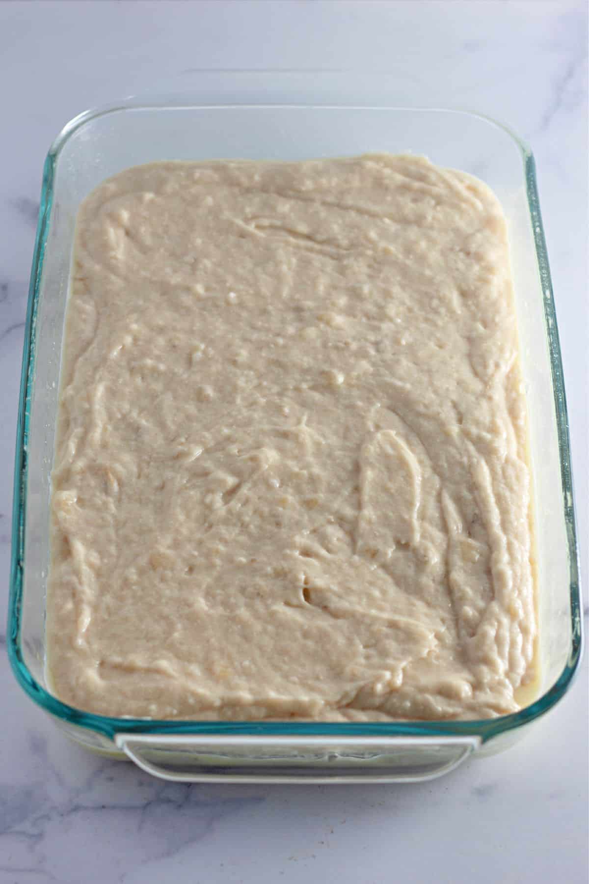 cake batter in a greased glass baking dish ready for the oven.