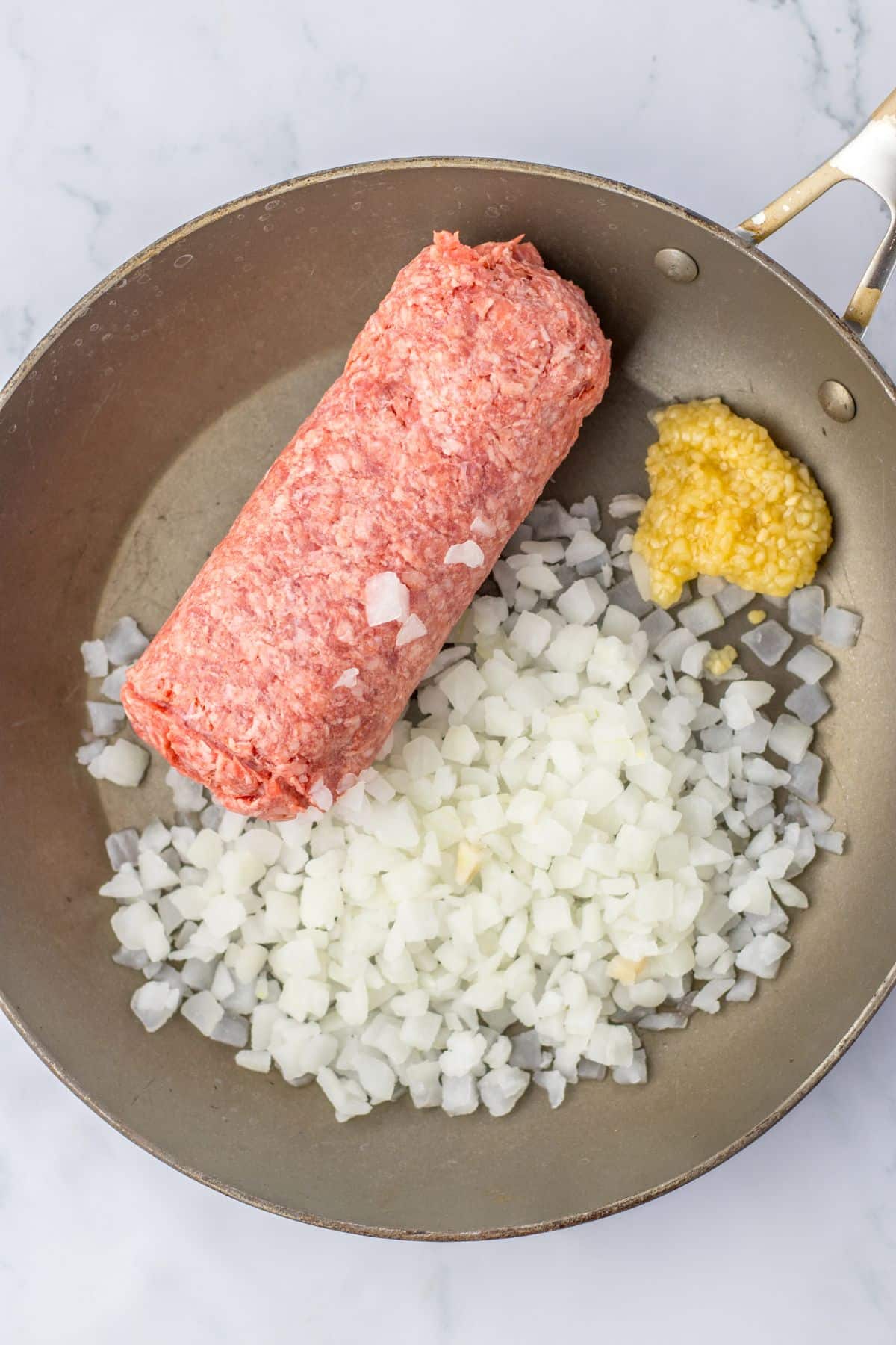 ground beef, onions, and garlic being cooked in a large skillet.