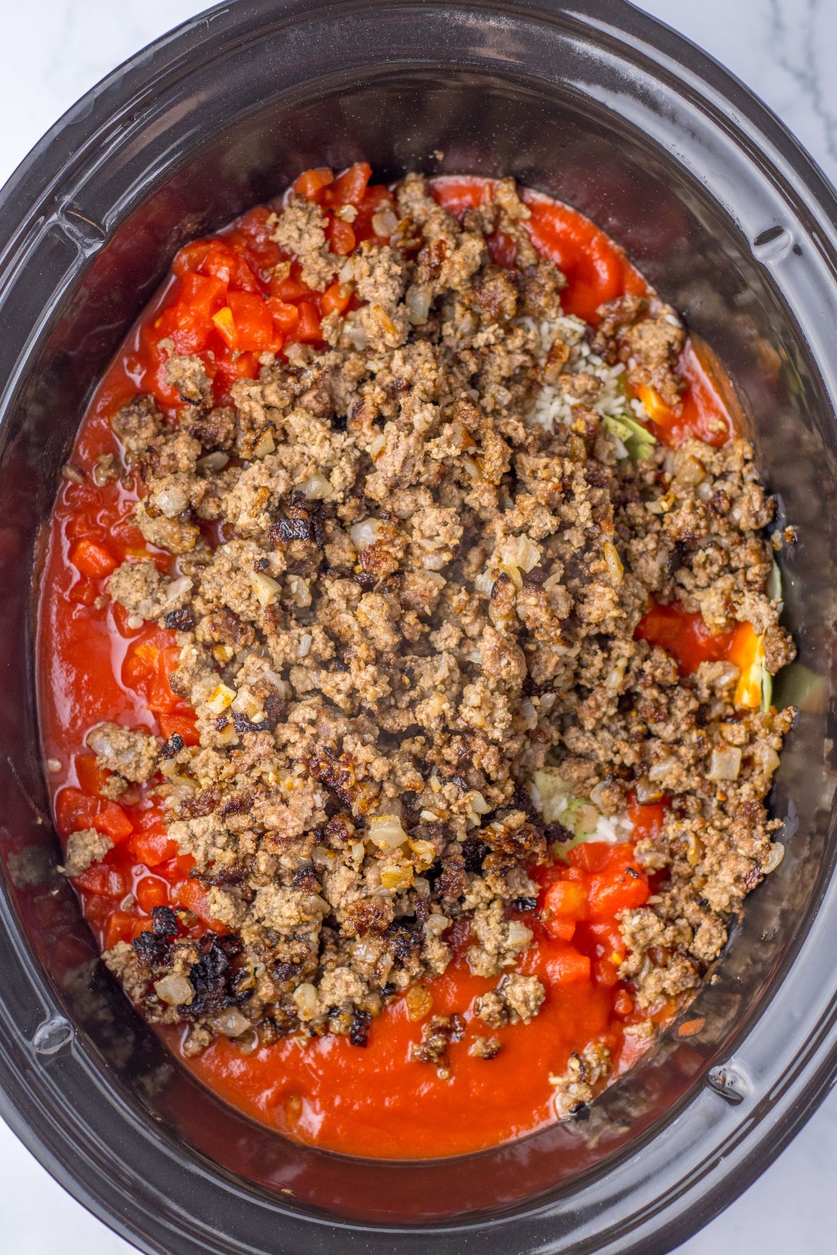 cooked ground beef and onions being added to a slow cooker.