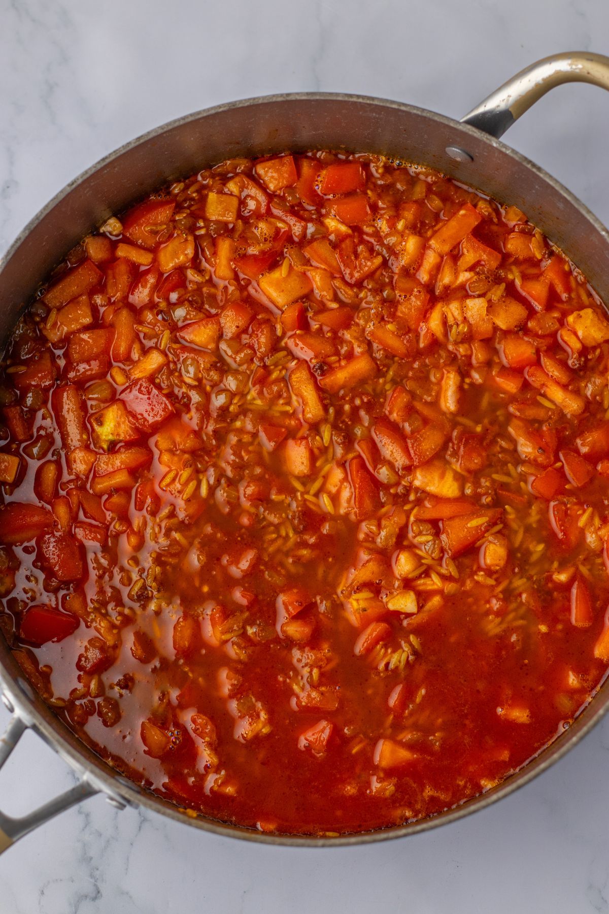 tomatoes, sausage, and onions being cooked in a large skillet.