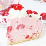 slice of chocolate cherry pie topped with whipped cream and a cherry on a plate.