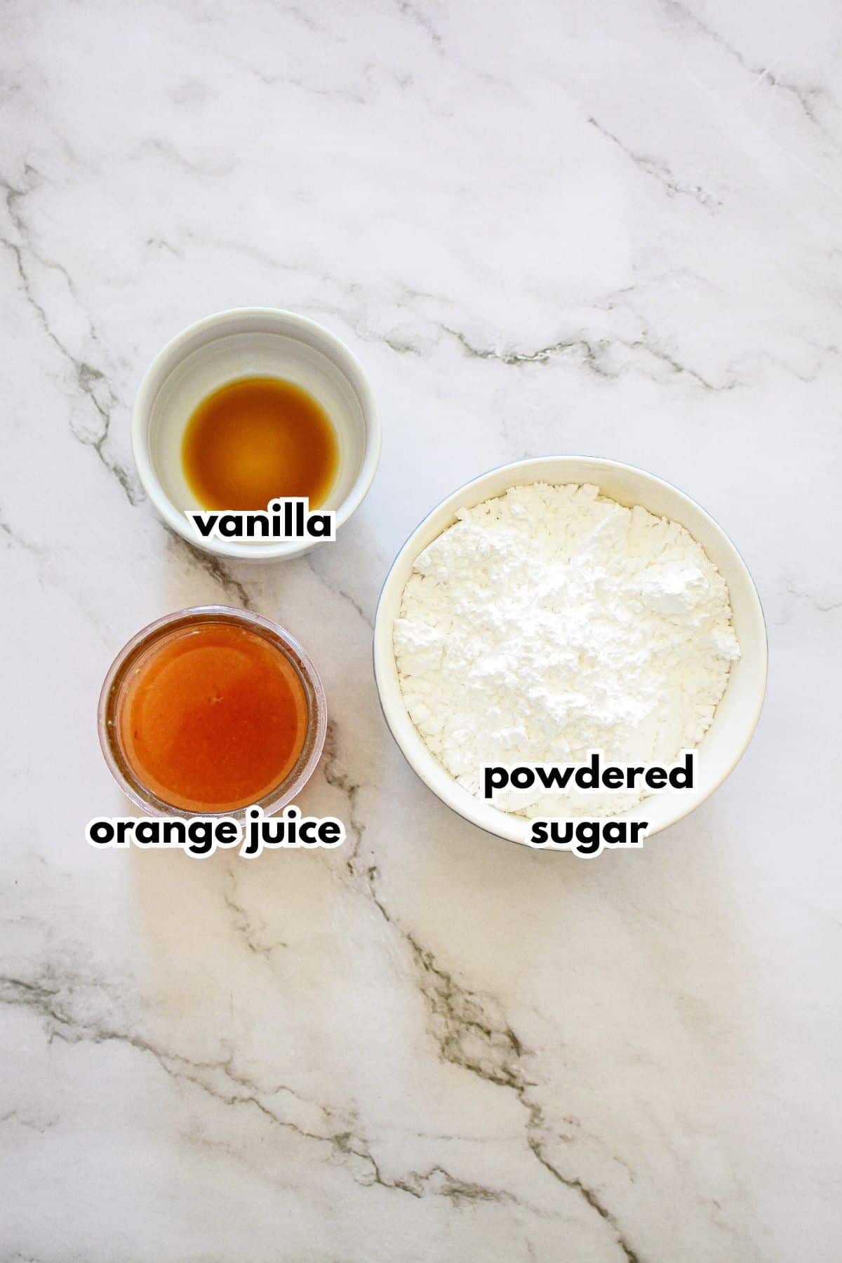 bowls of vanilla, orange juice, and powdered sugar on a marble counter.