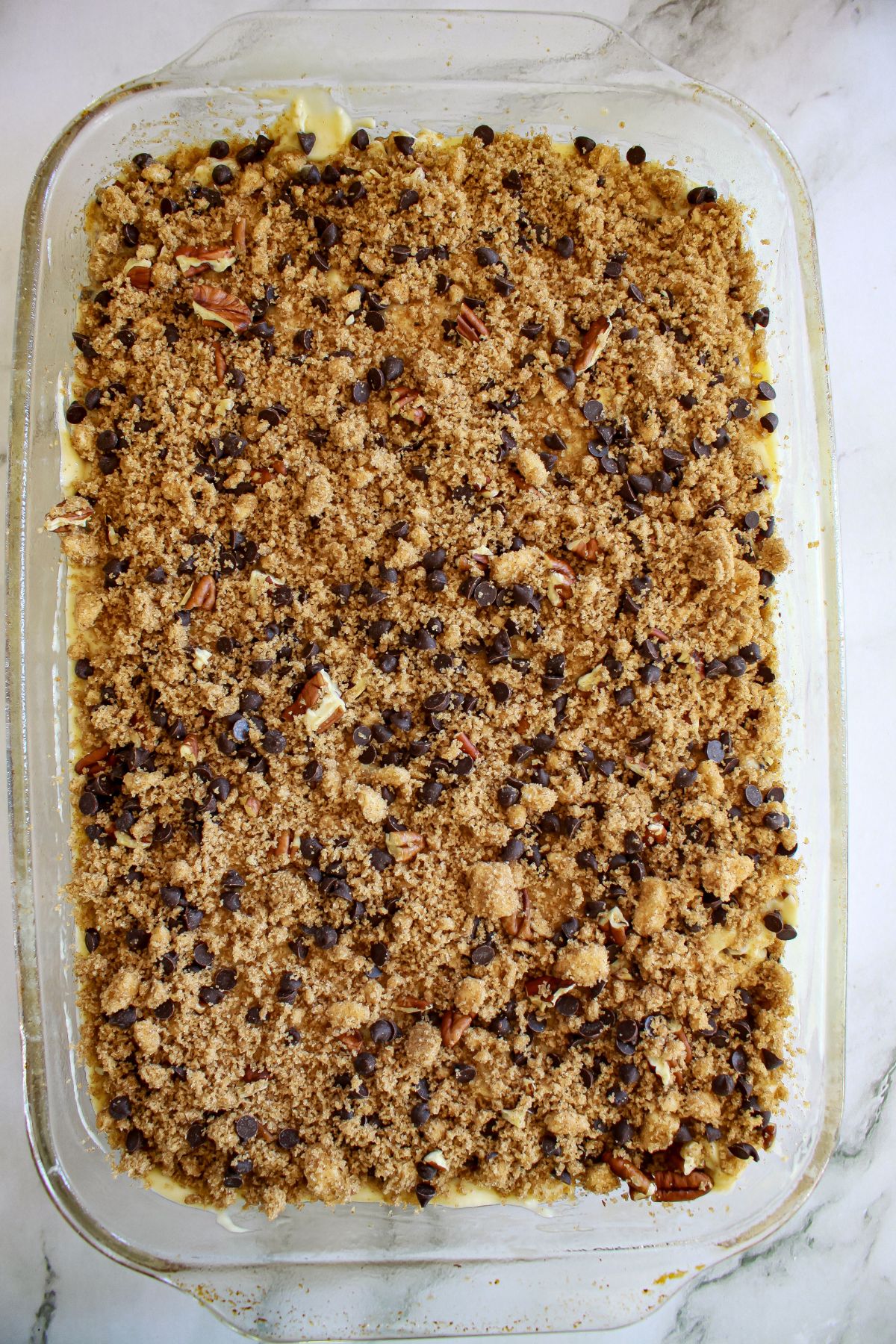 crumb topping being added to the top of a cake in a glass casserole dish.