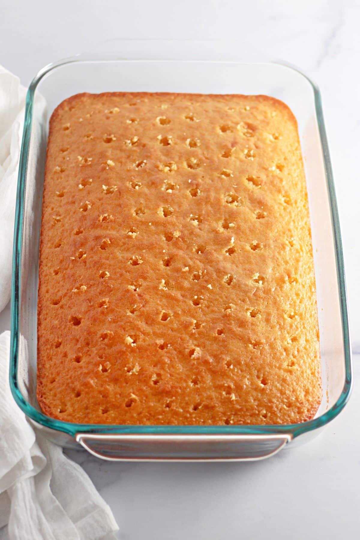 baked cake with holes poked in it in a glass casserole dish.