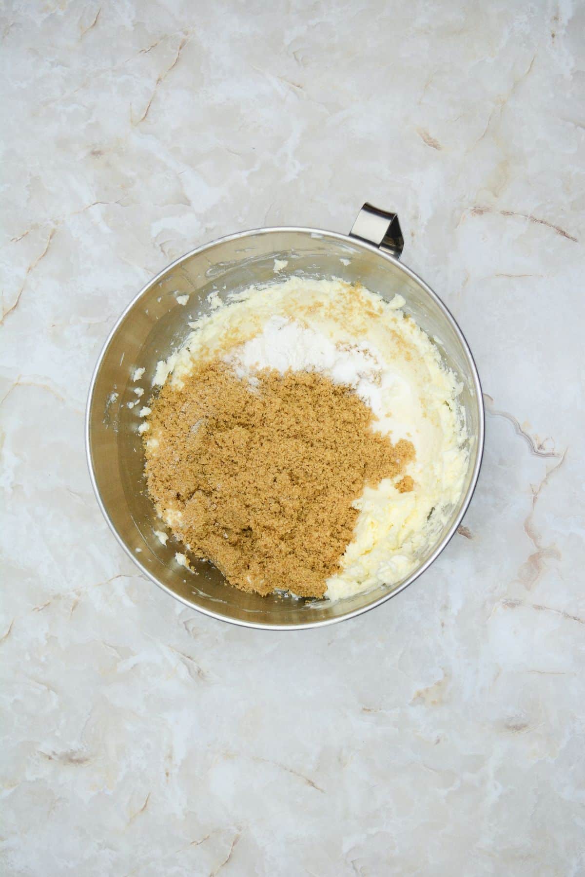 brown sugar, and flour being mixed into dough in a stainless steel mixing bowl.