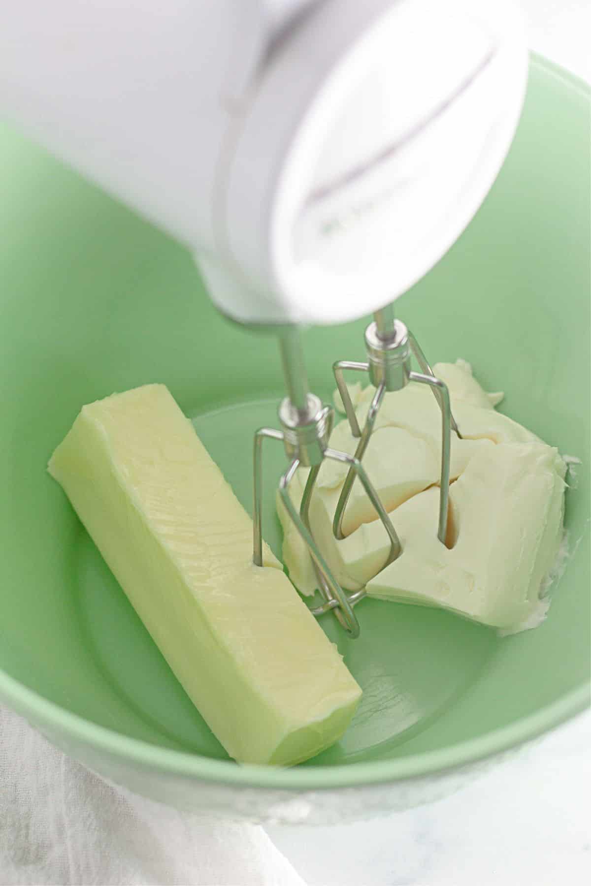 butter and cream cheese being creamed together with a hand mixer in a large bowl.